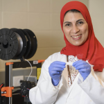 Rasha Elkanayati holds up her dry mouth strip product with lab equipment in background.