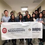 11 students stand for a group photo, holding banner with school and organization logo